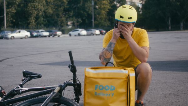 A food delivery worker beside his bike with his head in his hands