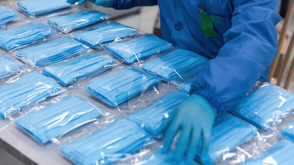 Gloved worker sorting packages of medical masks
