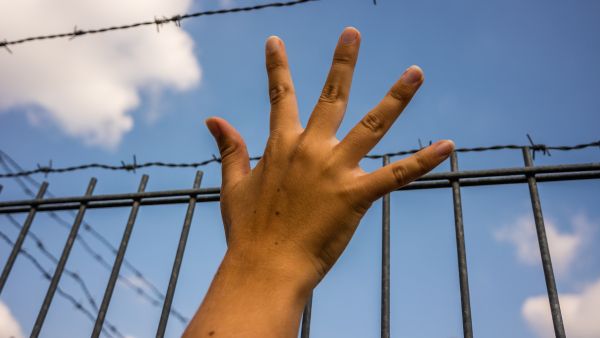 refugee child hand at US Mexico border wall