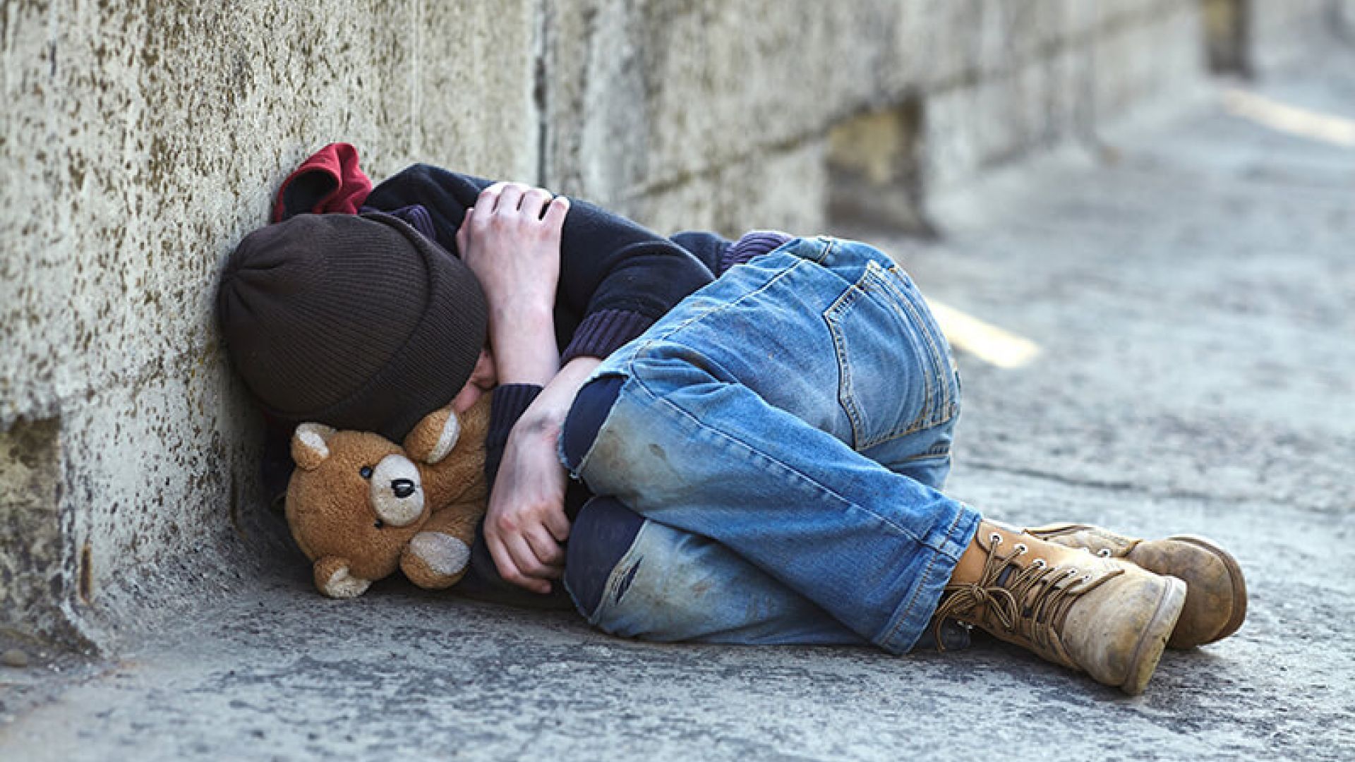 Child lying in street with teddy bear