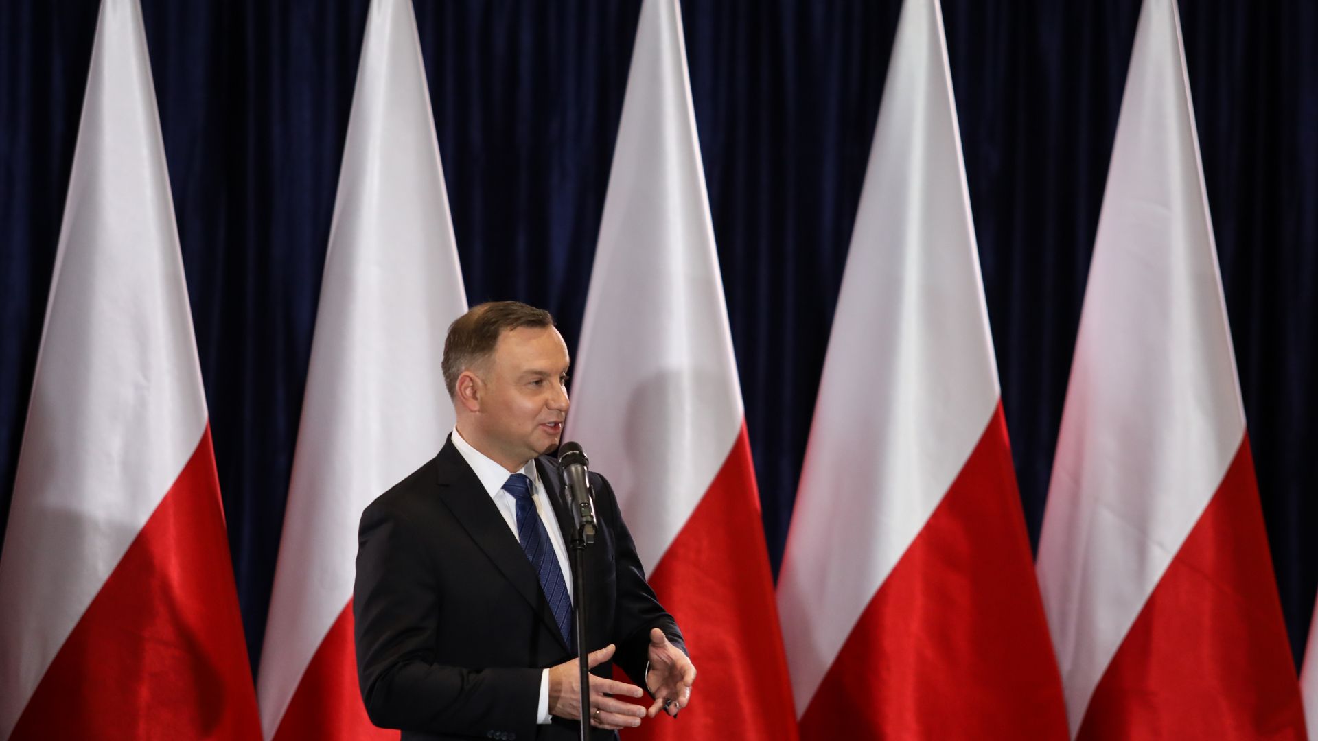 Polish president Andrzej Duda speaking in front of a row of Polish flags