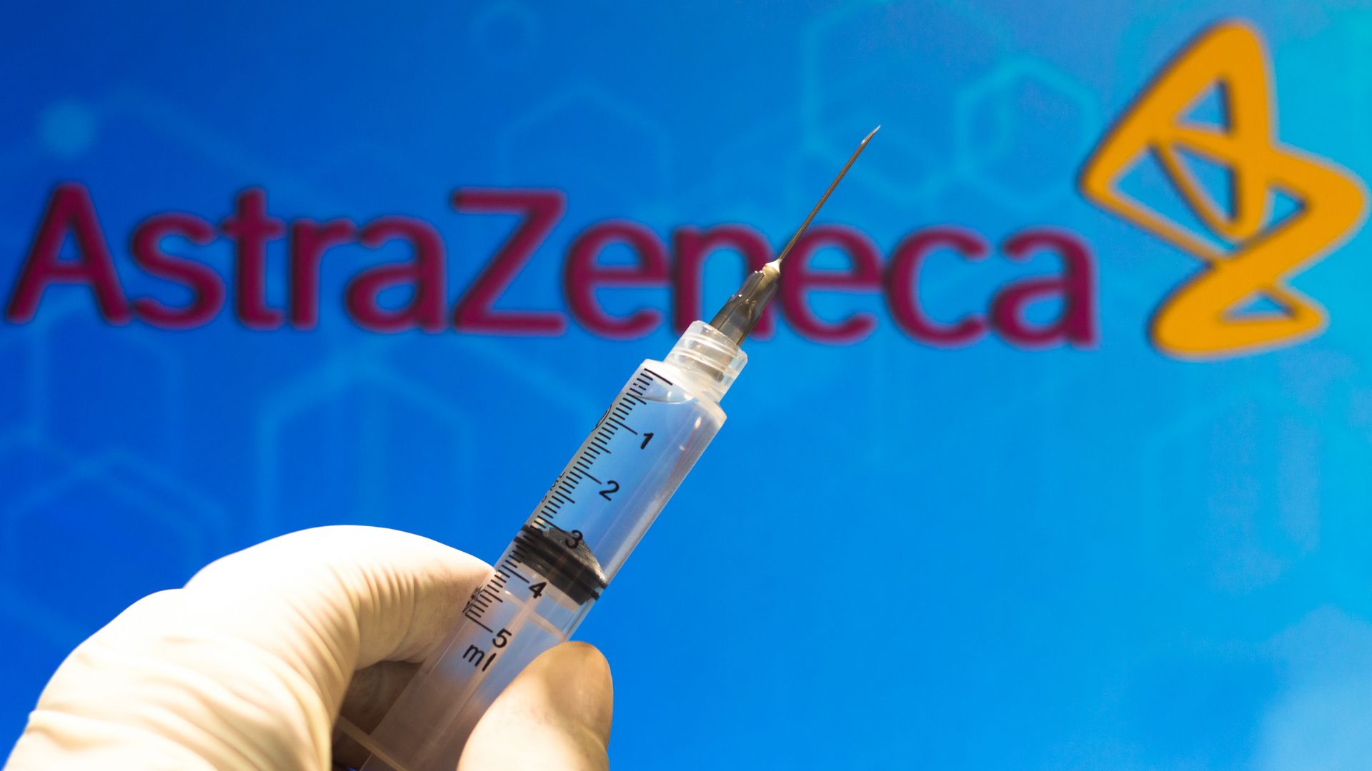 Syringe ready for vaccination in front of an AstraZeneca logo