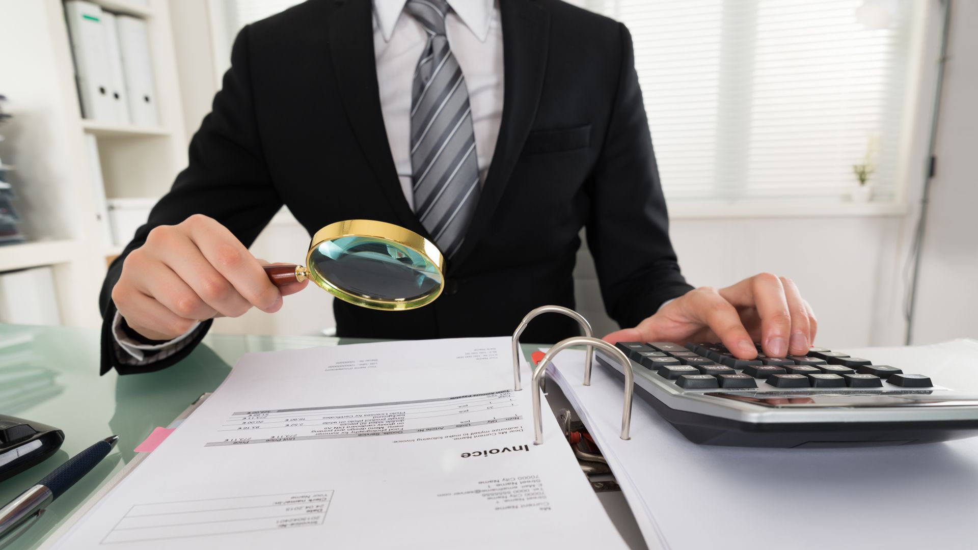 man looking at bills with magnyfying glass and calculator