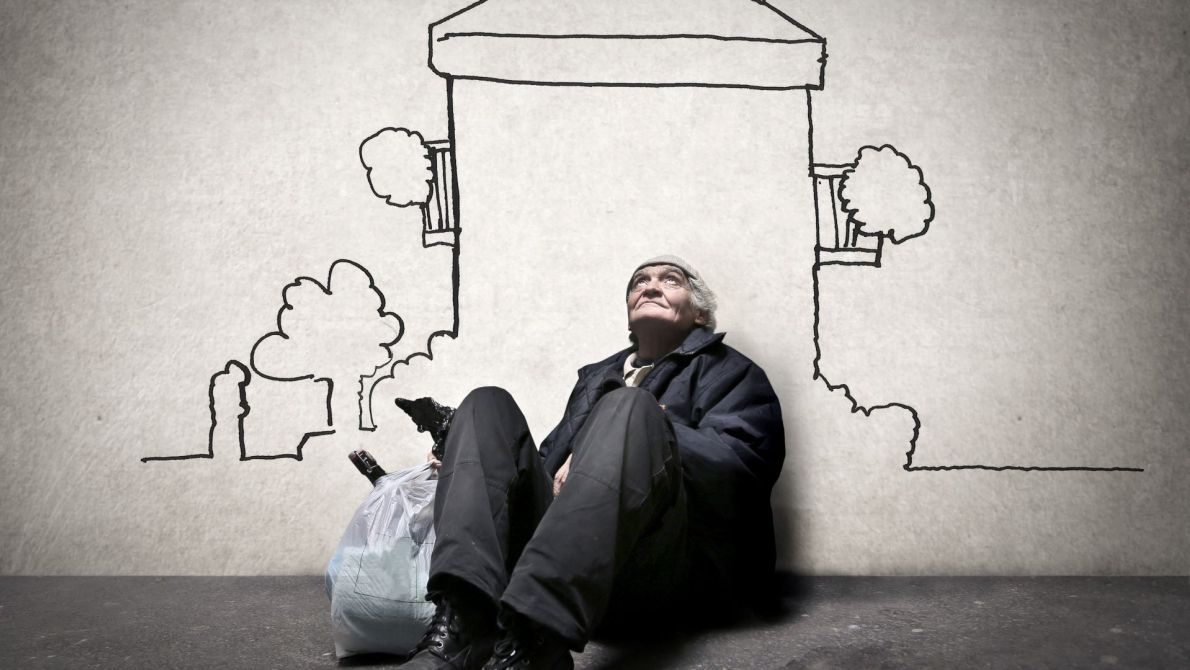 Homeless sitting in front of wall with a drawn house on it