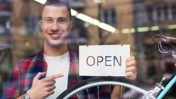 Smiling bike shop owner holding 'open' sign