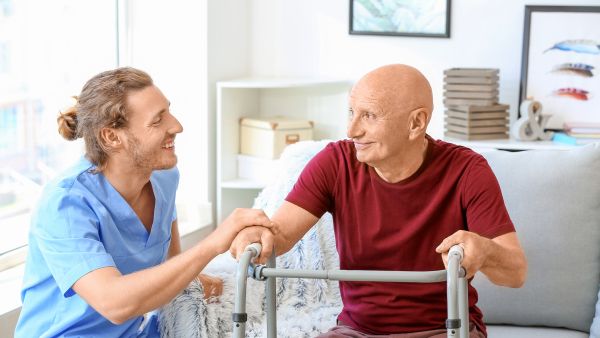 Young male carer helping an elderly man with a walking frame