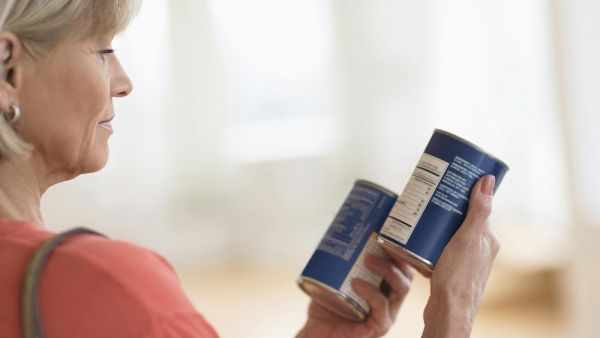 Lady holding 2 tins of food looking at labels